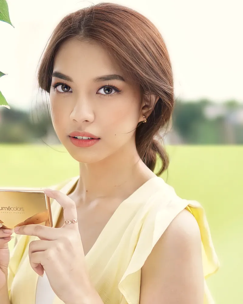 Model bergaun kuning di taman memegang Lumécolors Compact Powder emas