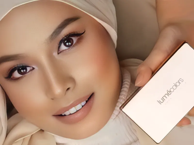 Model berhijab krem dengan riasan natural flawless tersenyum sambil memegang Lumécolors Compact Powder