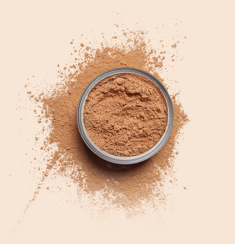 Jar Loose Powder terbuka dilihat dari atas, bubuk bedak berwarna tan bertebaran di sekelilingnya
