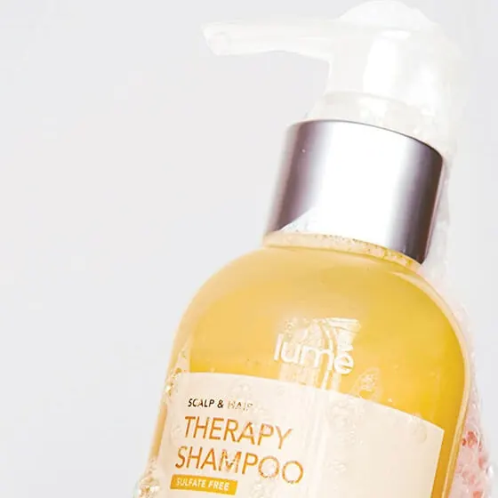 Tangan berbusa memegang botol Therapy Shampoo 150 mL